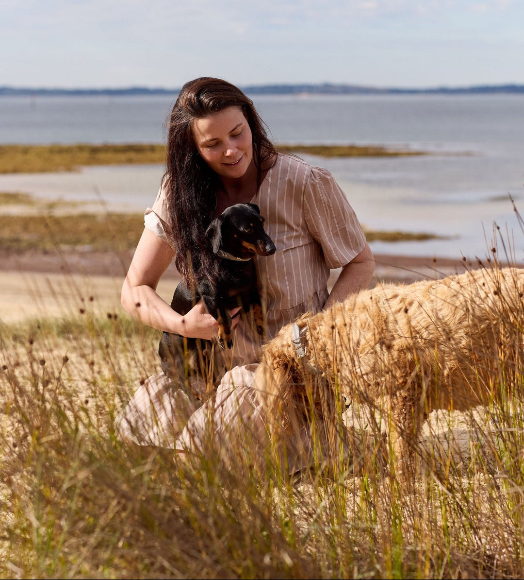 Sophie sitting on a grassy area by a body of water with her beloved dogs.