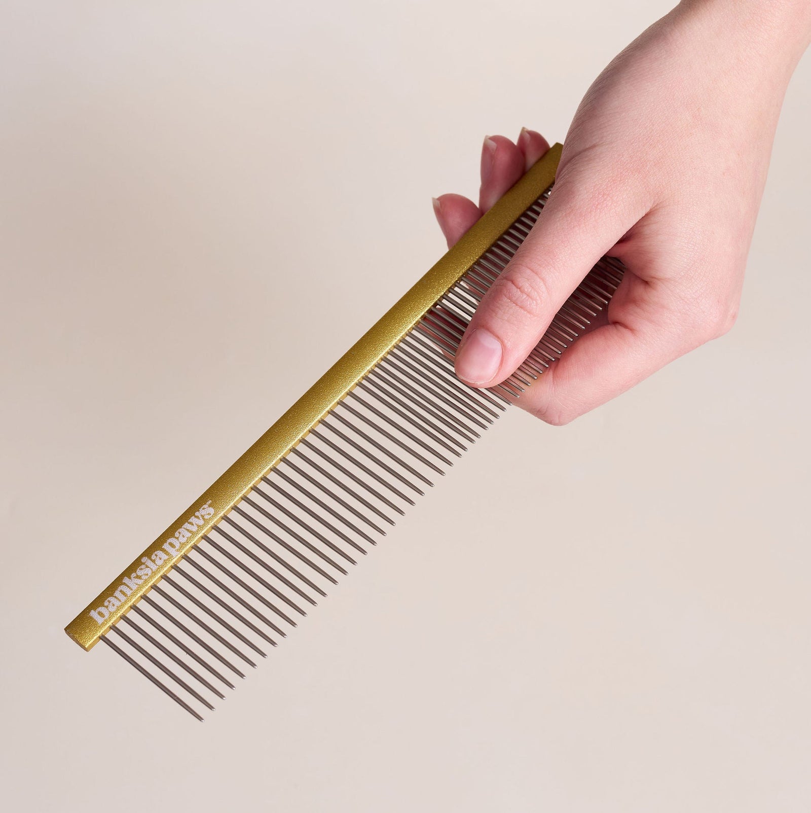 Hand holding a gold comb against a beige background