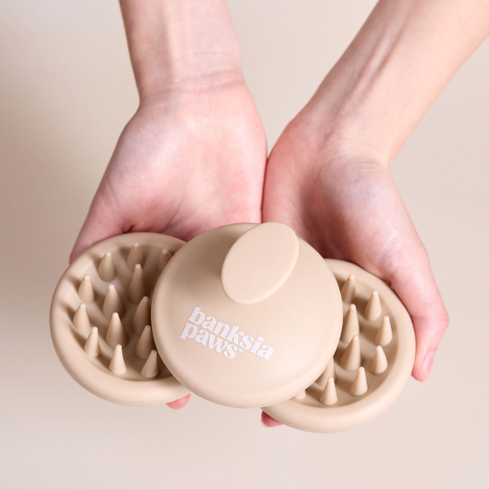 Person holding a beige pet Silicone Scrub Brush with 'Banksia Paws' branding against a neutral background